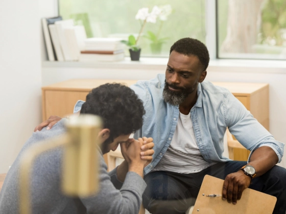Alcohol Rehab Services London. An image of a consultation with a young adult male client, the mid adult male therapist reaching out to get his attention and offer support.
